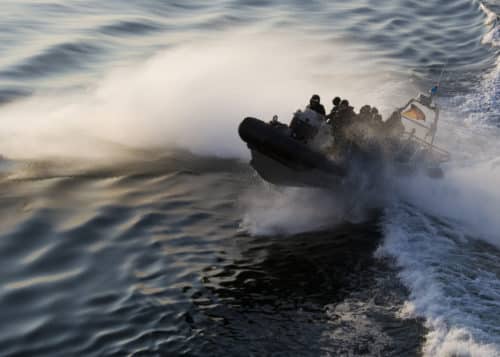 Special forces in inflatable rigid hull boat hitting the wake of a ship and creating a lot of spray.